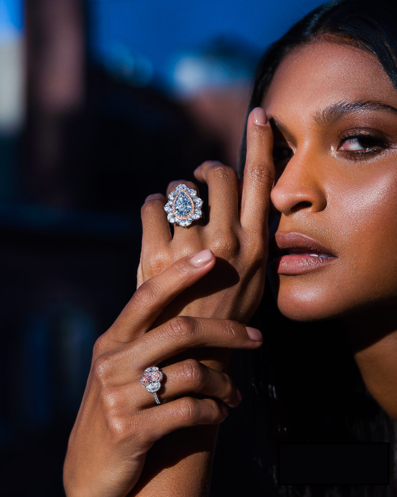 A portrait of a model from 3/4 view wearing two blue diamond rings