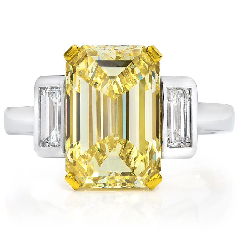 An emerald cut yellow diamond ring with two smaller colorless emerald cut diamonds on each side.